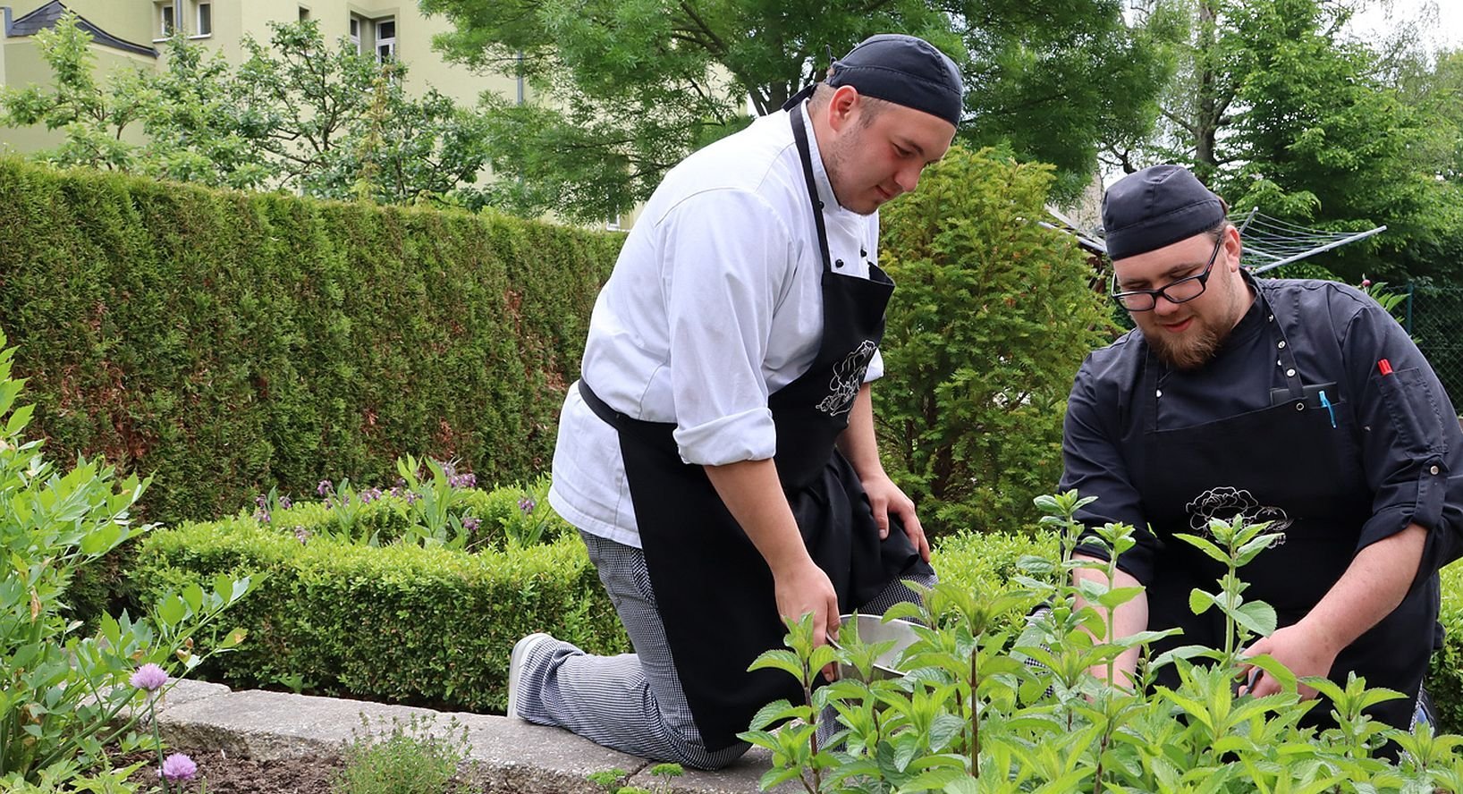 Zwei Männer in Schürze machen Gartenarbeit.