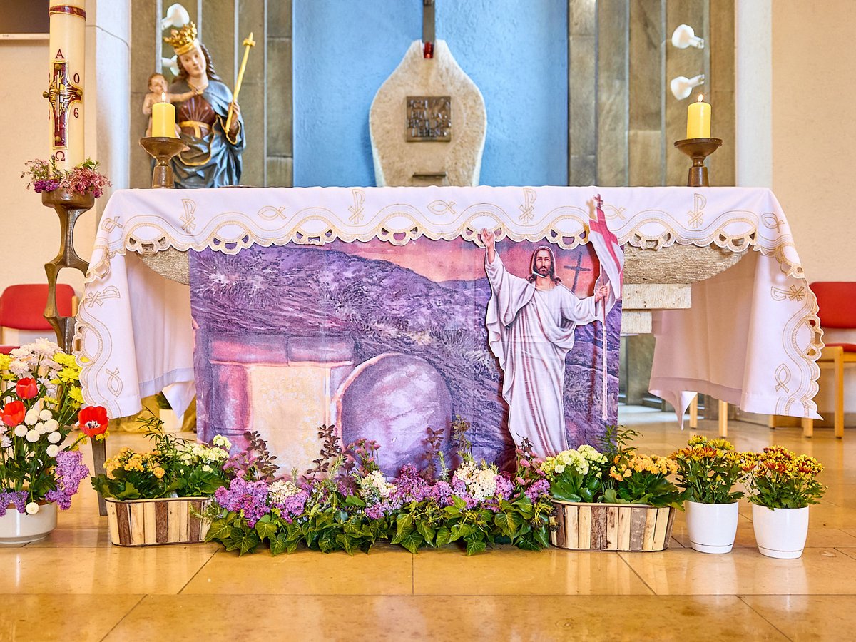 Ein festlich geschmückter Kirchenaltar mit Osterkerze, Blumen und einem Banner des auferstandenen Jesus.