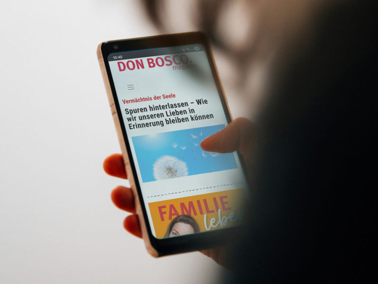 Hand hält Smartphone mit einem Artikel aus dem 'DON BOSCO magazin' über Spuren und Erinnerungen.