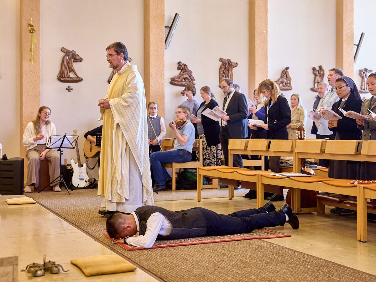 Ein Mann liegt bei einer religiösen Zeremonie vor einem Priester auf dem Boden, während die Gemeinde dahinter steht.