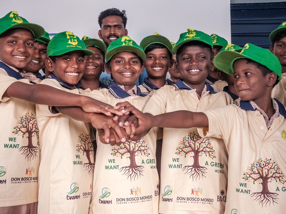 Lächelnde Don Bosco Schüler in grünen Kappen und "We Want A Green World"-Shirts, die Hände als Zeichen der Einheit stapeln.