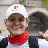 Zwei lächelnde Männer, einer im Don Bosco T-Shirt, zeigen Daumen hoch vor einer Stadtkulisse.